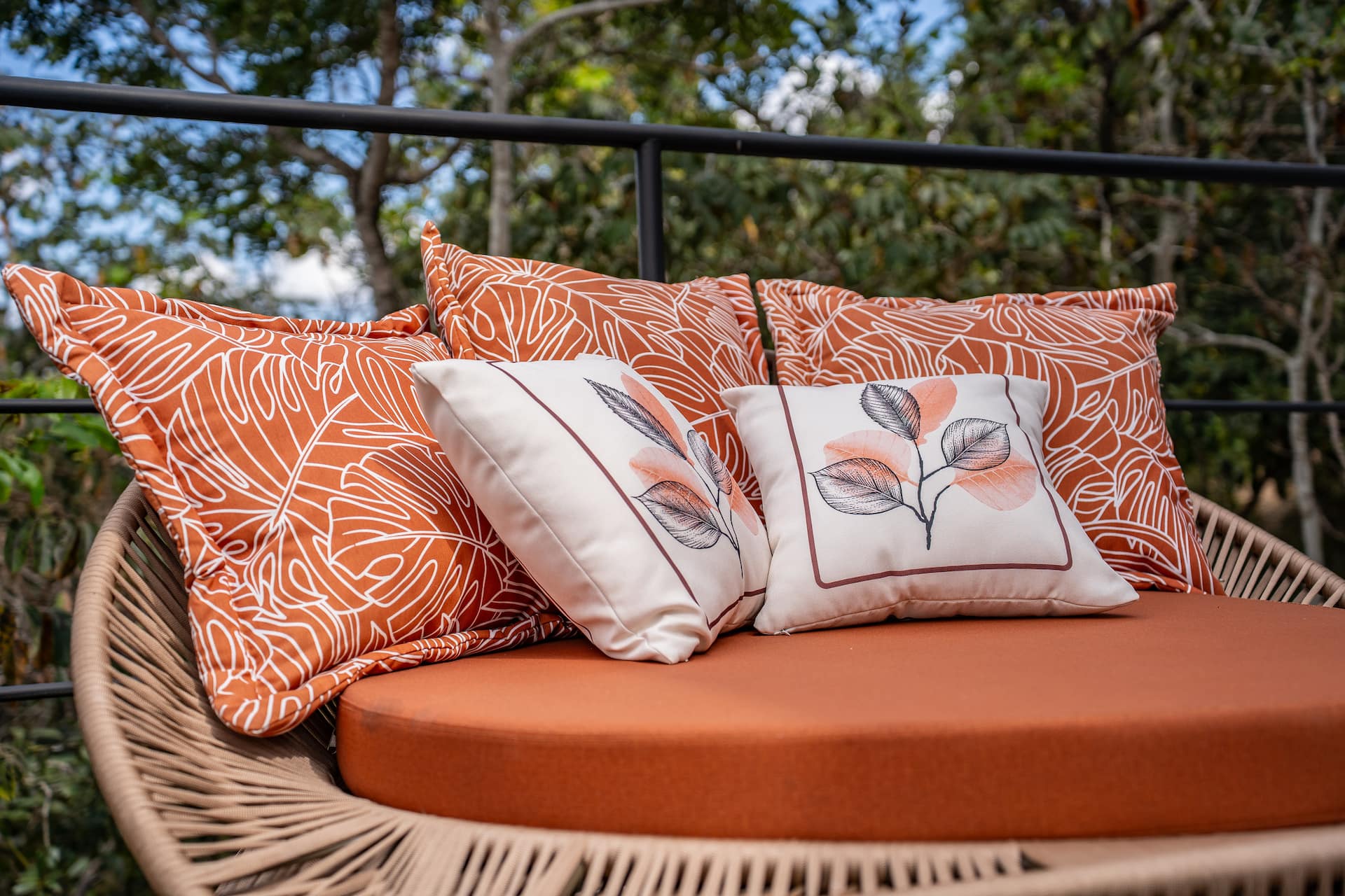 Almofadas estampadas em laranja e branco sobre a namoradeira de vime no deck