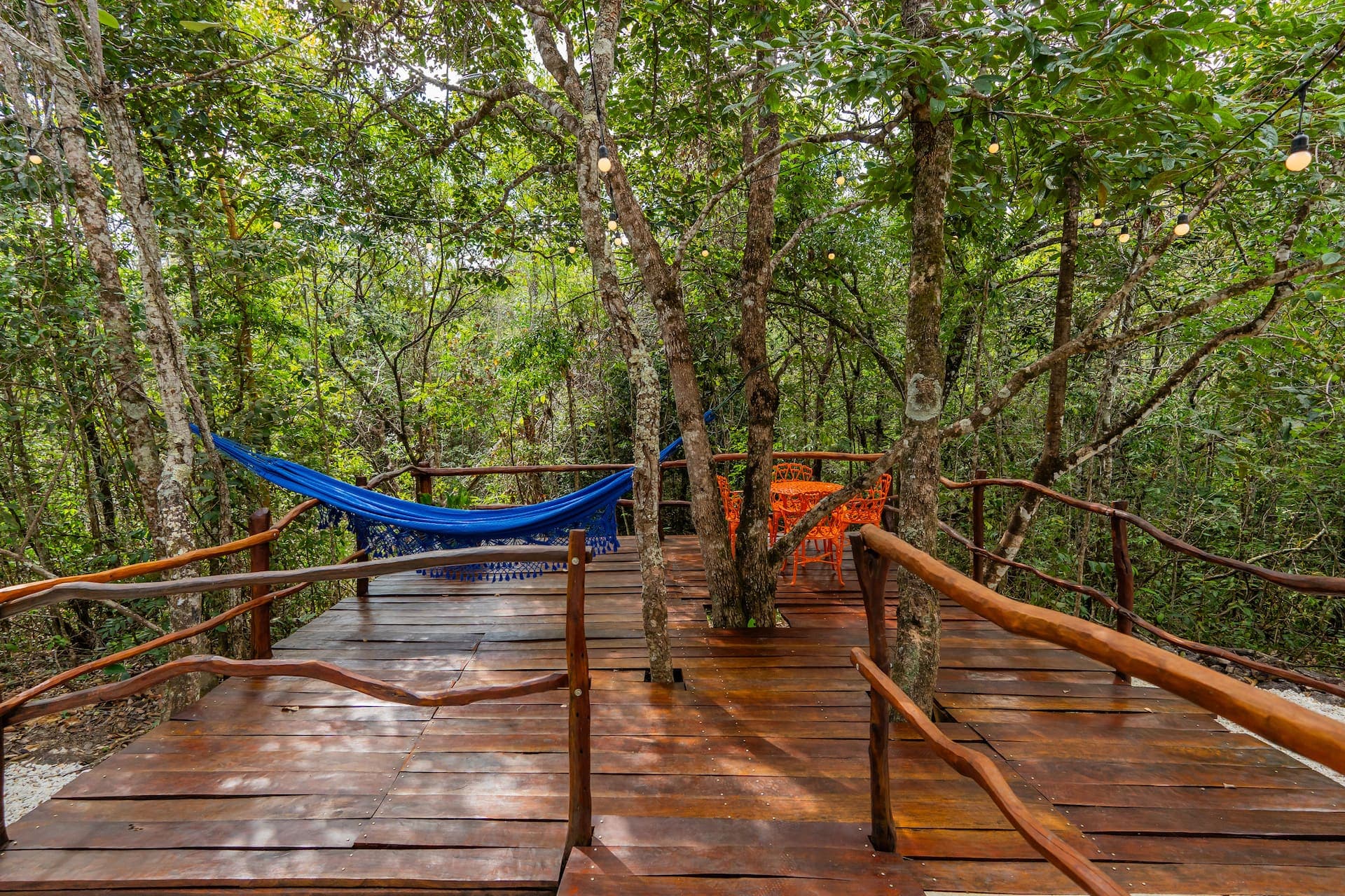 Passarela de madeira entre as árvores, com rede azul e luzinhas decorativas