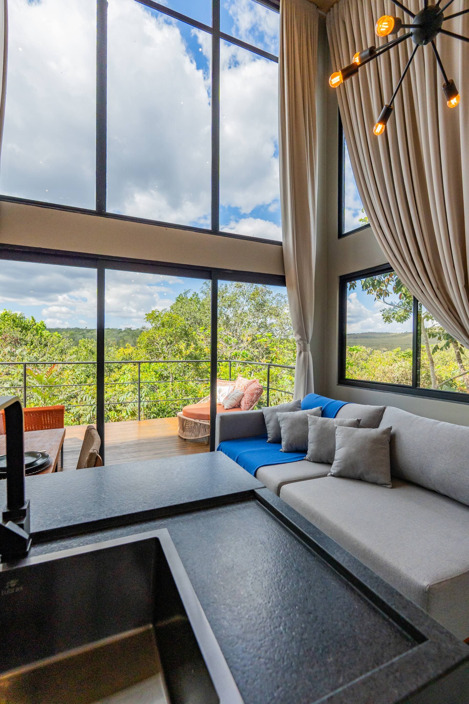 Sala de estar vista da bancada da cozinha, com sofá cinza e azul e varanda com espreguiçadeira