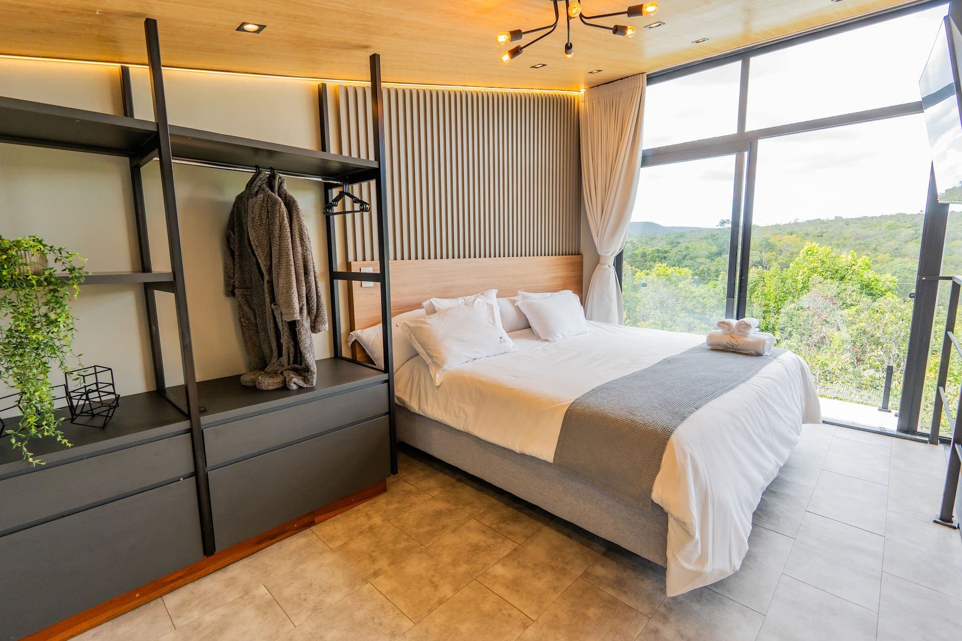 Quarto com roupão pendurado no closet aberto e cama king ao fundo