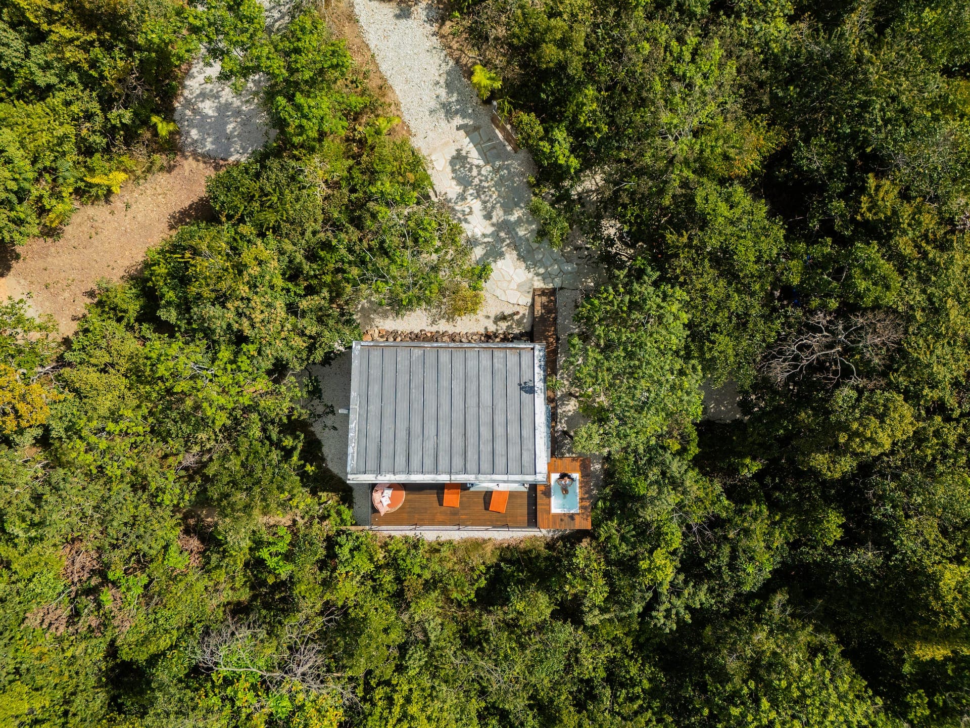 Vista aérea da tiny house cúbica cercada de mata fechada, com deck e hidromassagem