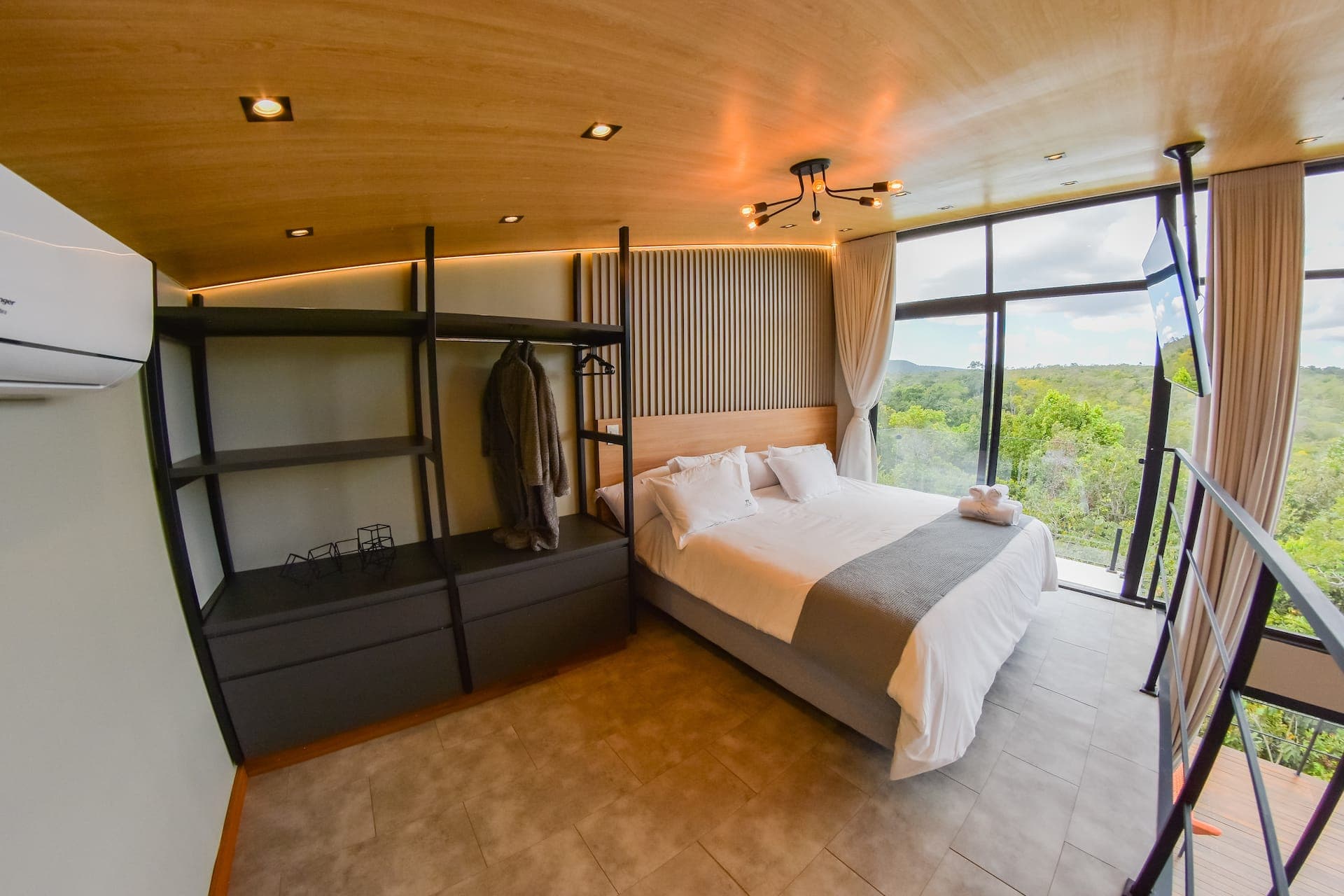 Quarto com cama king, cabeceira ripada, closet aberto e vista para a Serra dos Pireneus