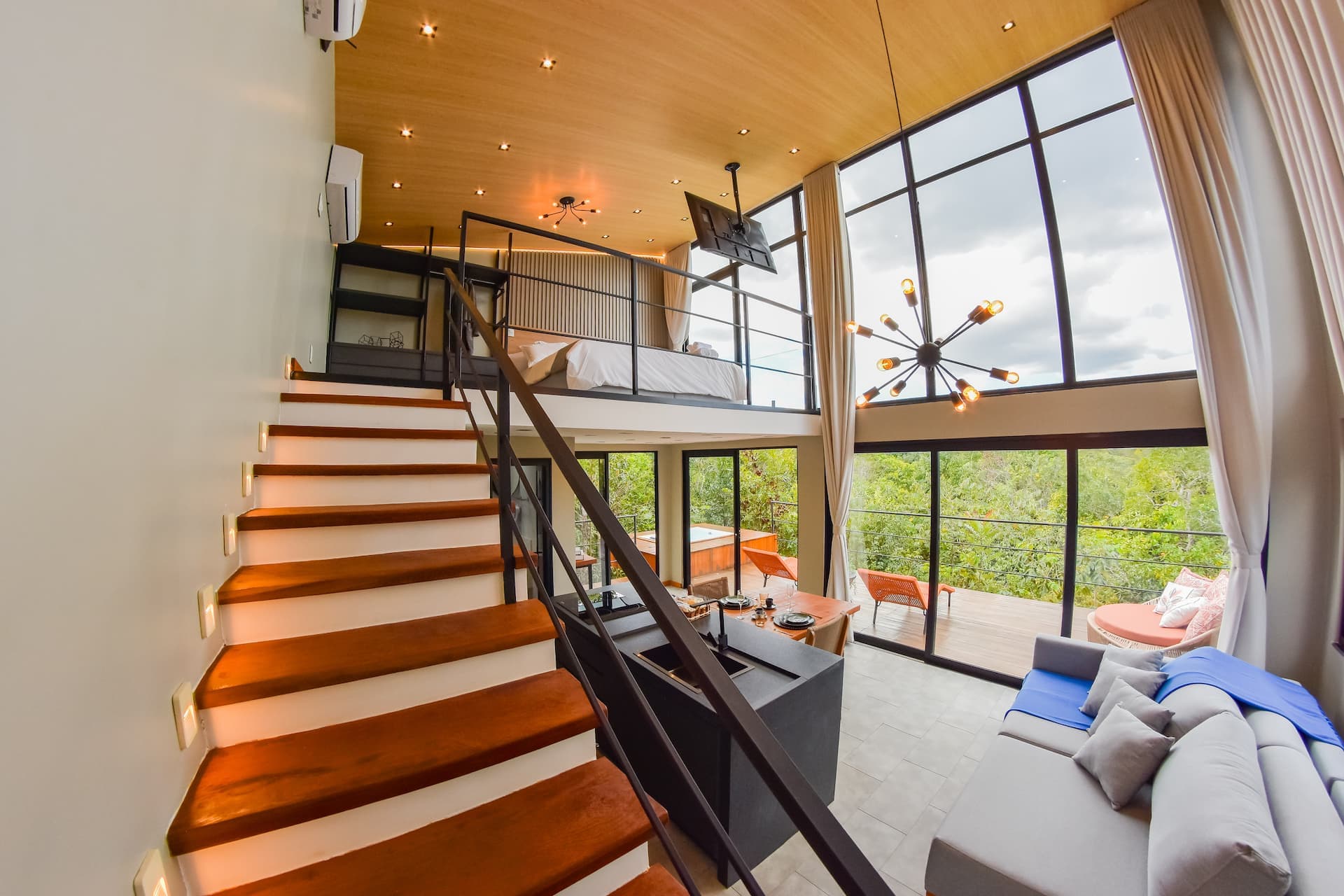 Sala em pé-direito duplo com mezanino do quarto, escada de madeira e vidraça panorâmica para a serra